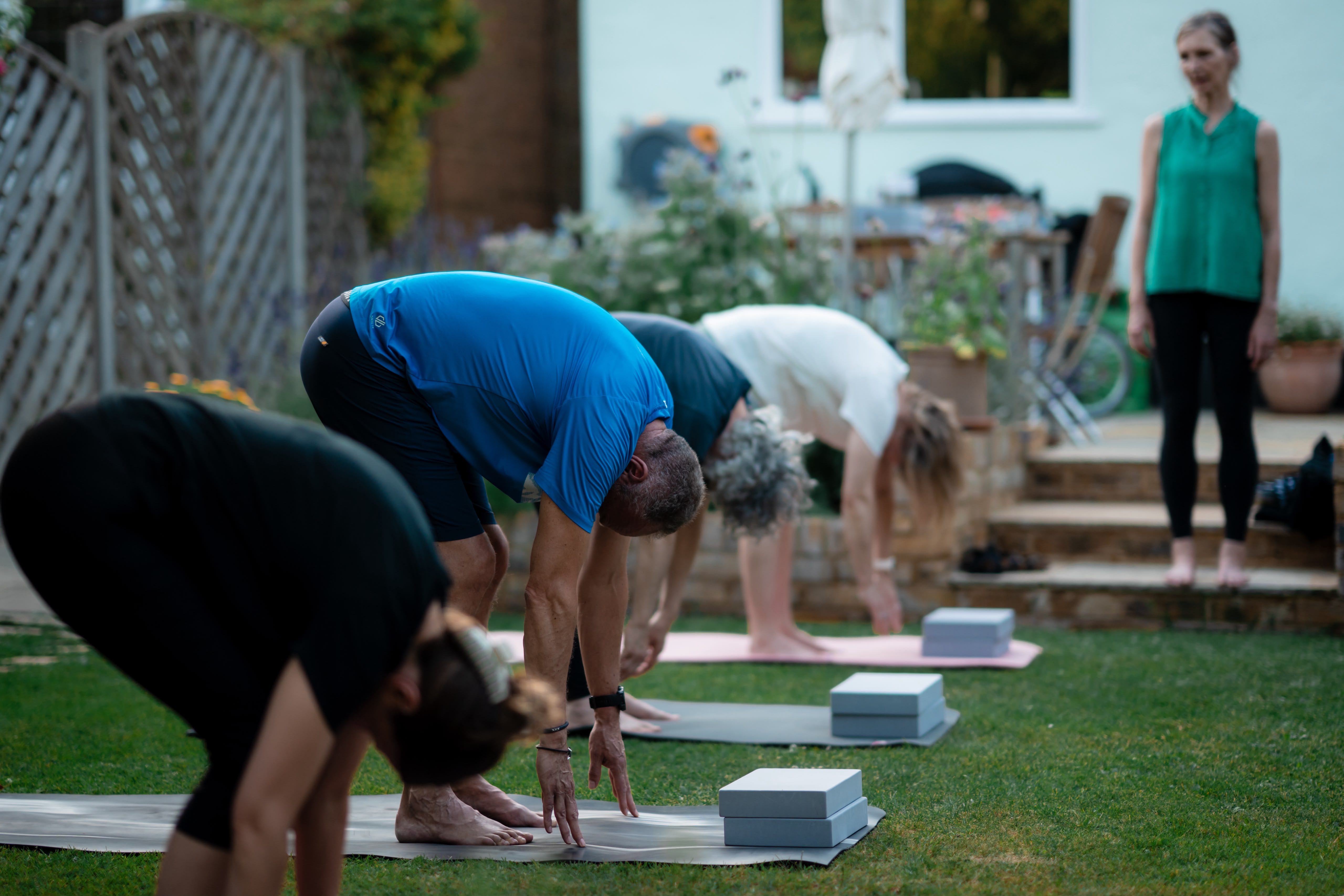 A group class practising standing forward bend (uttanasana) in a garden